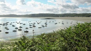 Un paysage côtier avec de nombreux bateaux ancrés dans des eaux calmes, une plage de sable et une colline boisée en arrière-plan.