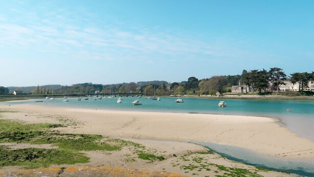 Une plage avec des bateaux, un rivage sablonneux et des bâtiments en arrière-plan.