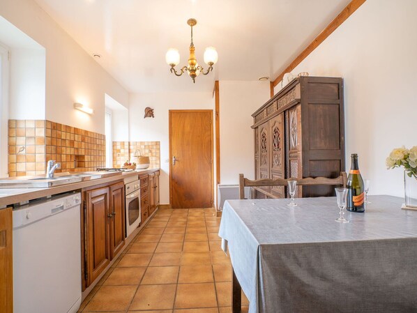 A kitchen with wooden cabinets, a tiled backsplash, a chandelier, and a dining area with a table set for two.
