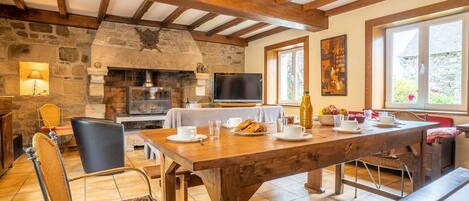 Un comedor rústico con chimenea de piedra, vigas de madera y una televisión.