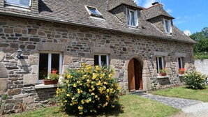 Une maison en pierre avec un toit en tuiles, de nombreuses fenêtres et une porte d’entrée.