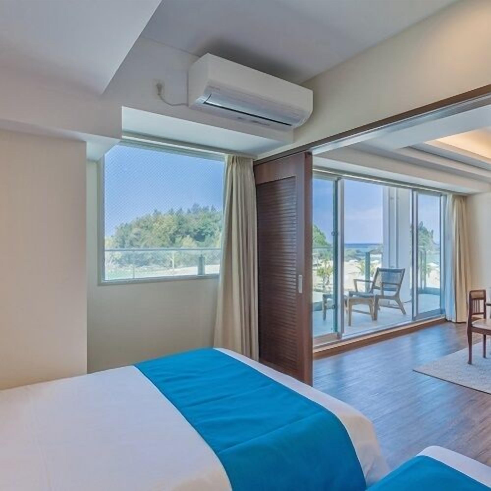 A hotel room with a bed, a large window, and a sliding glass door leading to an outdoor area.