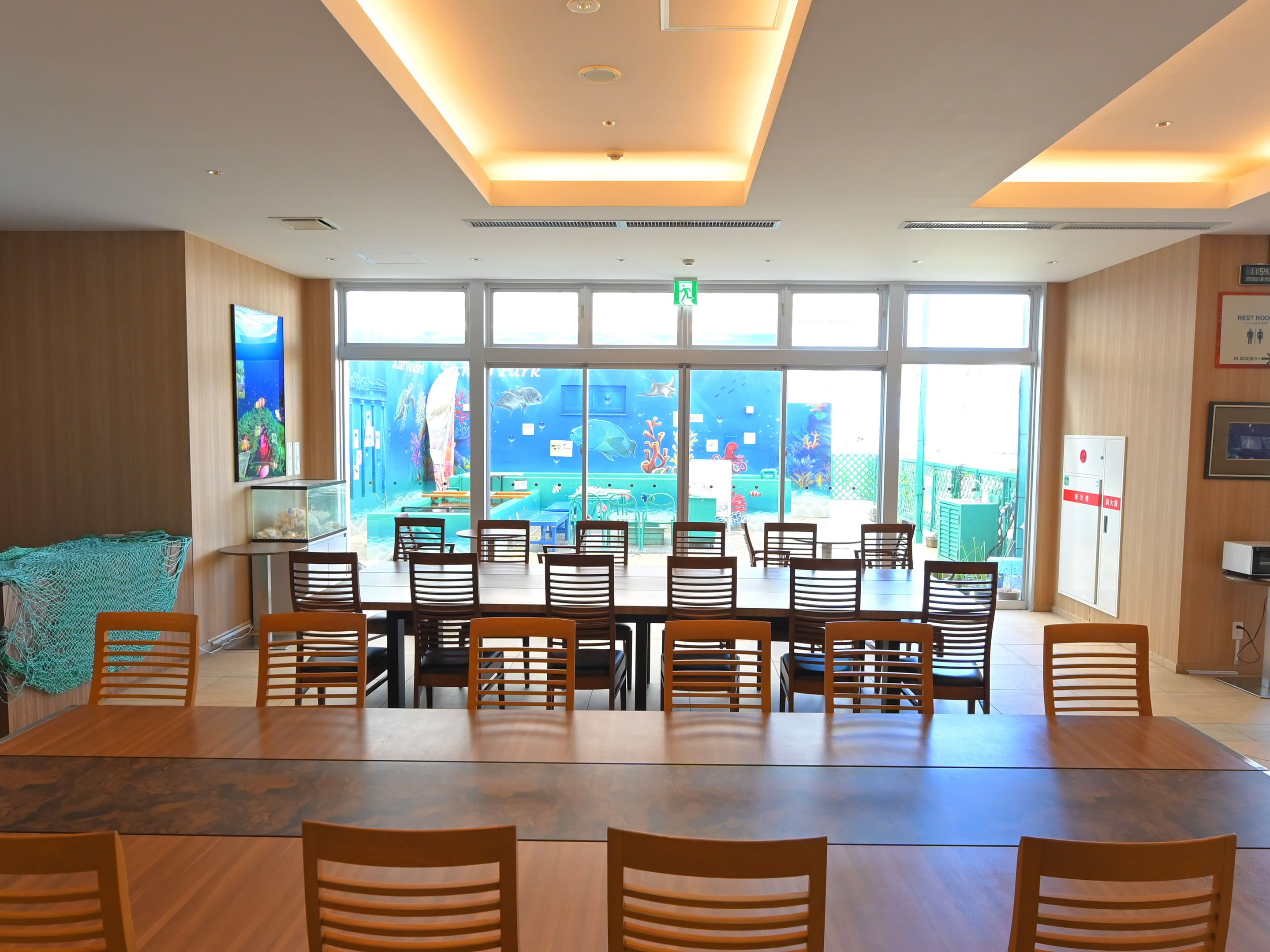 A conference room with a large table and chairs, a view of an aquarium through the windows, and a ceiling with recessed lighting.