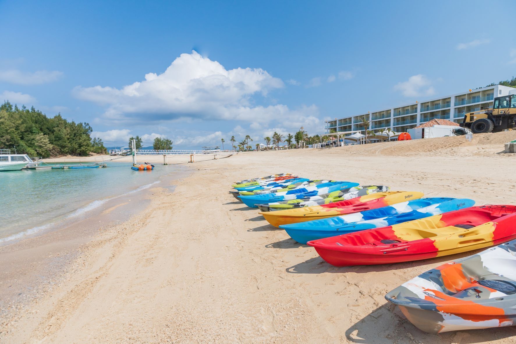 A beach with colorful kayaks lined up on the sand, a clear blue sky, and a building in the background.
