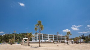 Un hotel de varios pisos, sombrillas exteriores y palmeras.