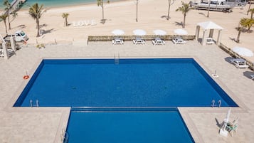 Una piscina con un cartel que dice 'LOVE' en la playa, sillas de descanso y un puesto de salvavidas.