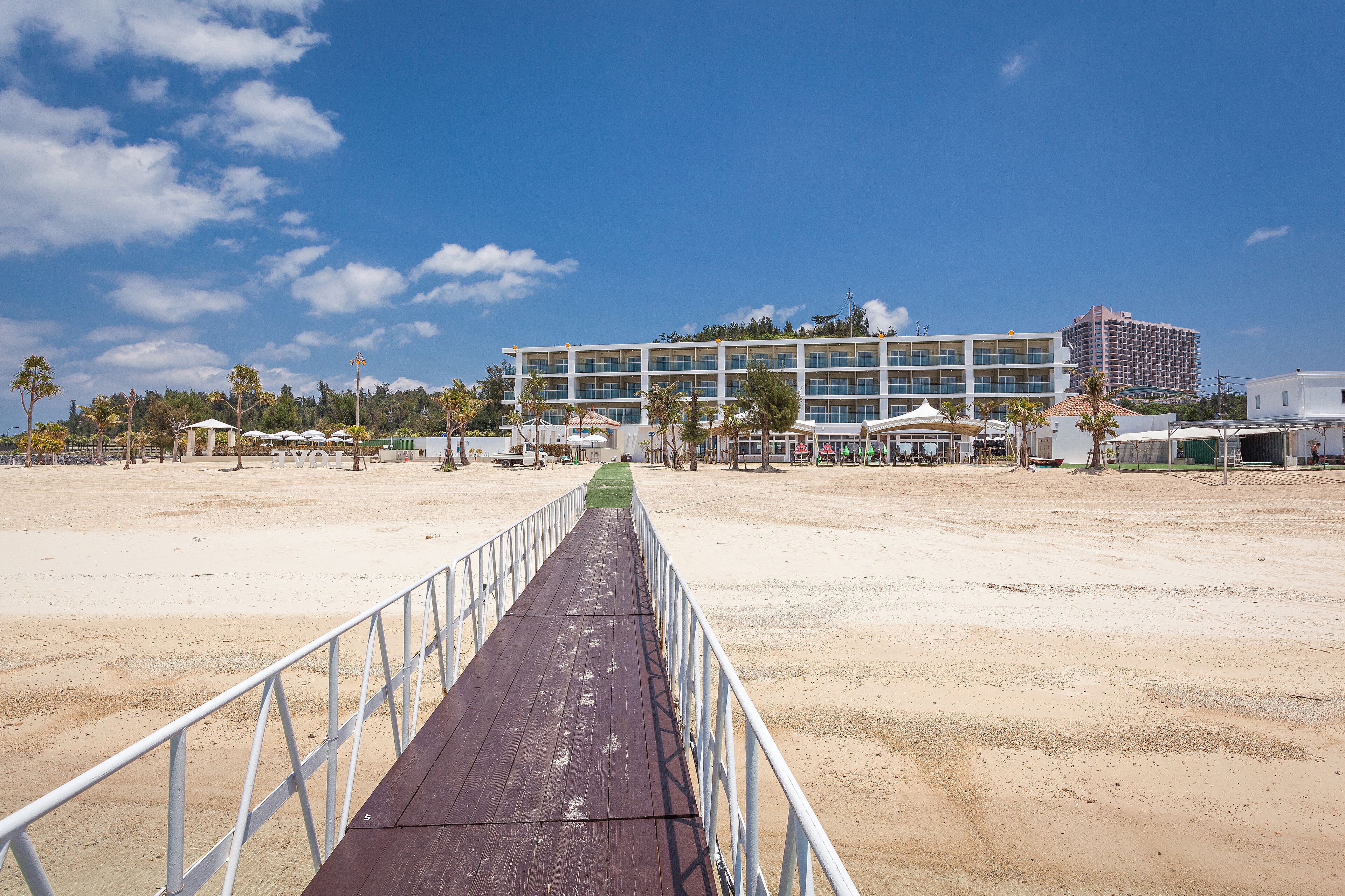Un paseo marítimo que lleva a un hotel con piscina y sombrillas de playa.
