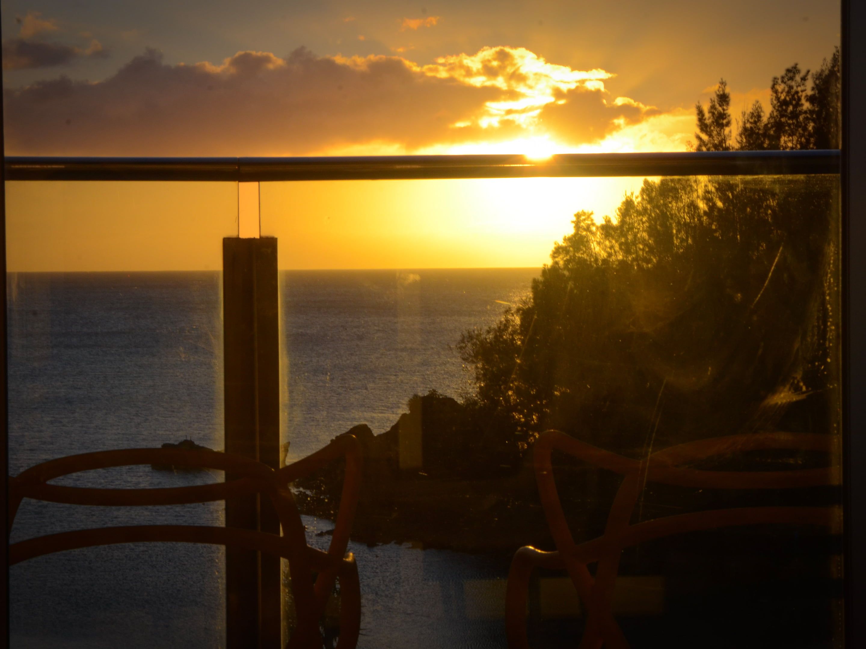 A sunset view through a window with a metal railing.