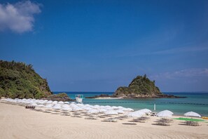 A beach with white umbrellas, a lifeguard tower, and a clear blue sky. - Kariyushi LCH Resort (Nago)