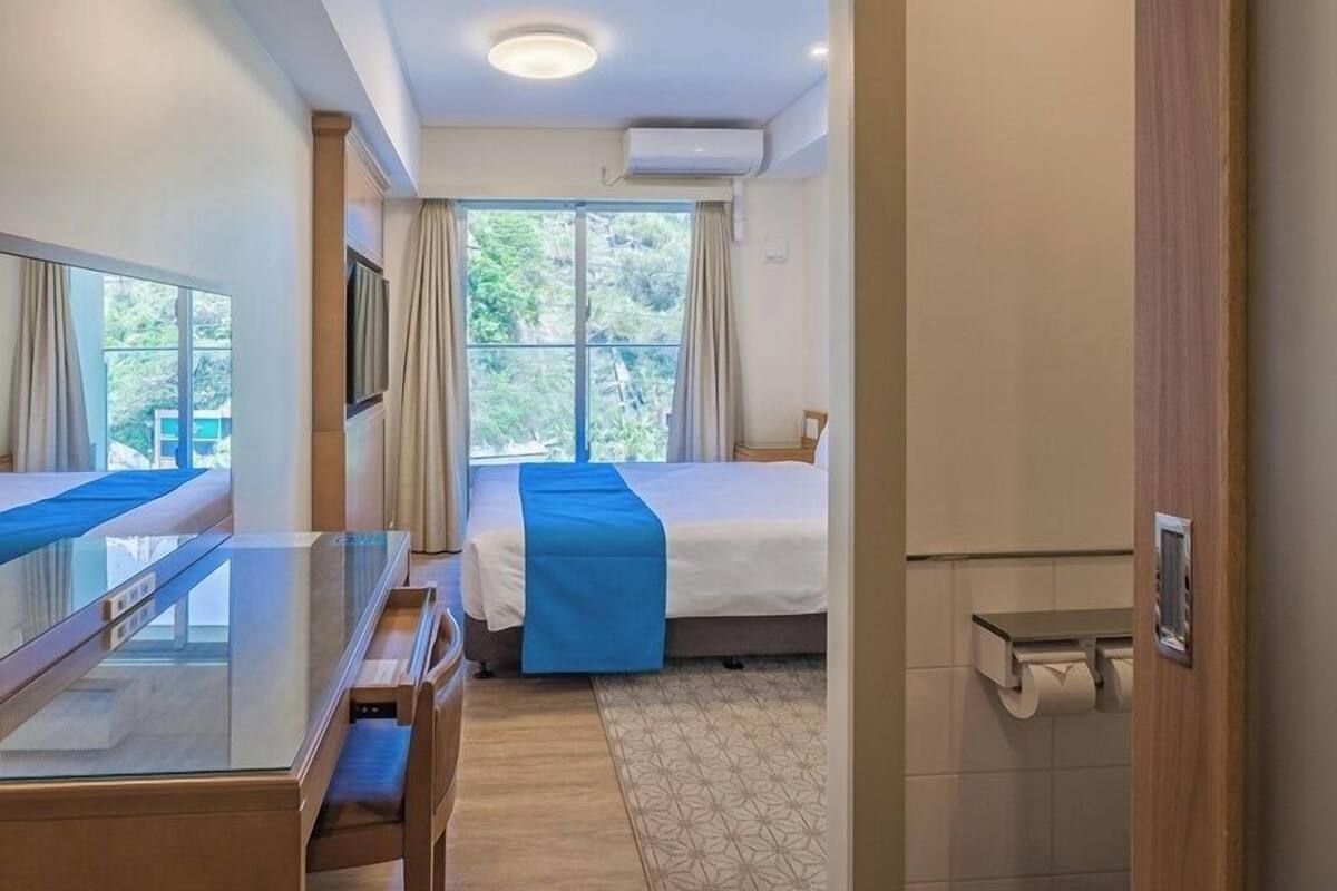 A hotel room with a bed, a desk, a chair, and a window with curtains.