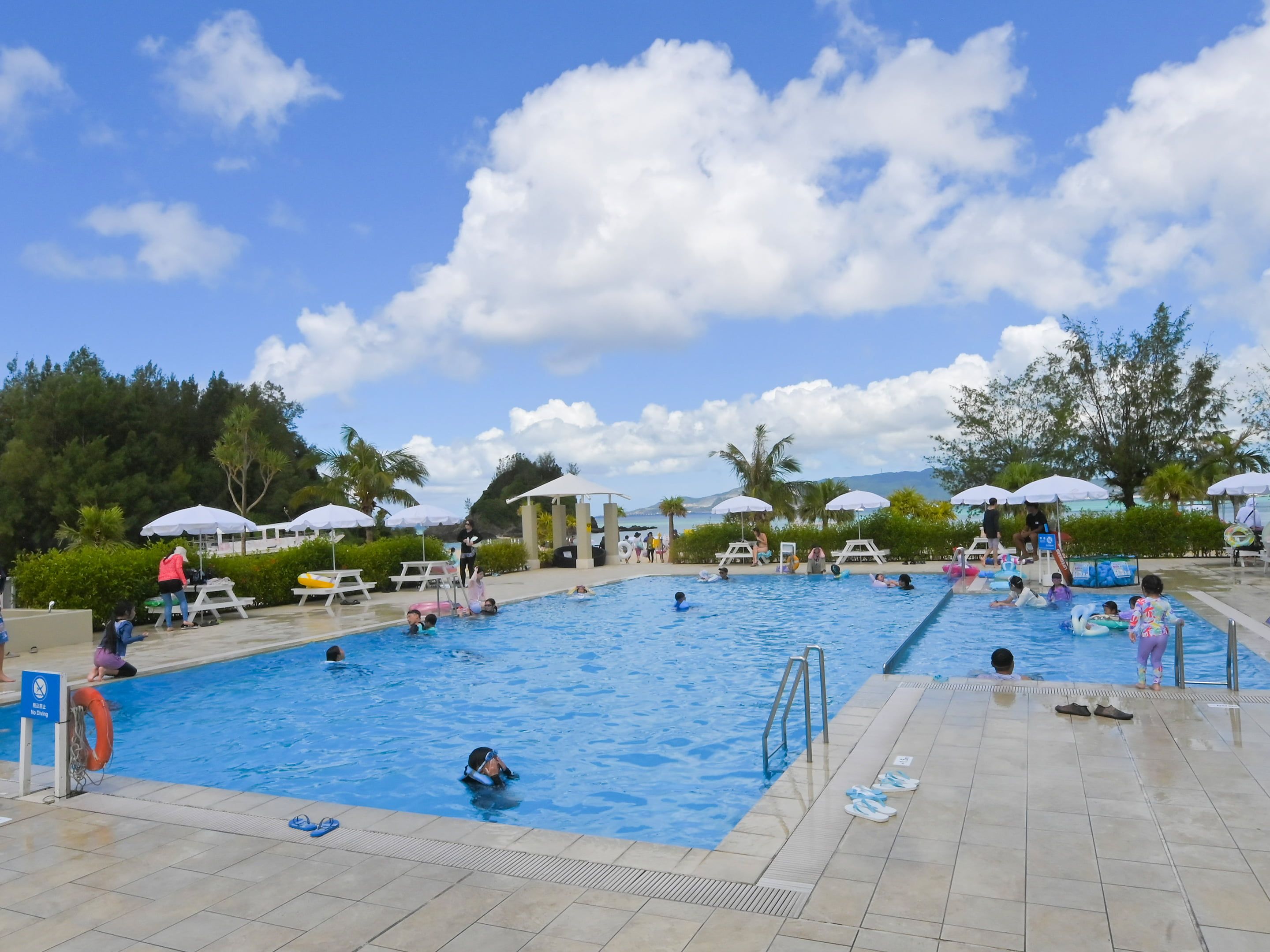A swimming pool with multiple lanes, surrounded by umbrellas and lounge chairs.