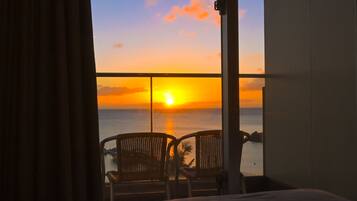 Una habitación con cama, dos sillones y vistas al atardecer sobre el mar.