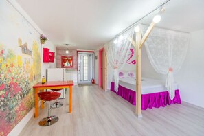 Una habitación con una cama, una mesa y una silla. Hay una puerta que da a otra habitación.