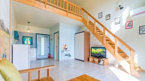 Een ruime woonkamer met een houten trap, een televisie en een keuken op de achtergrond.