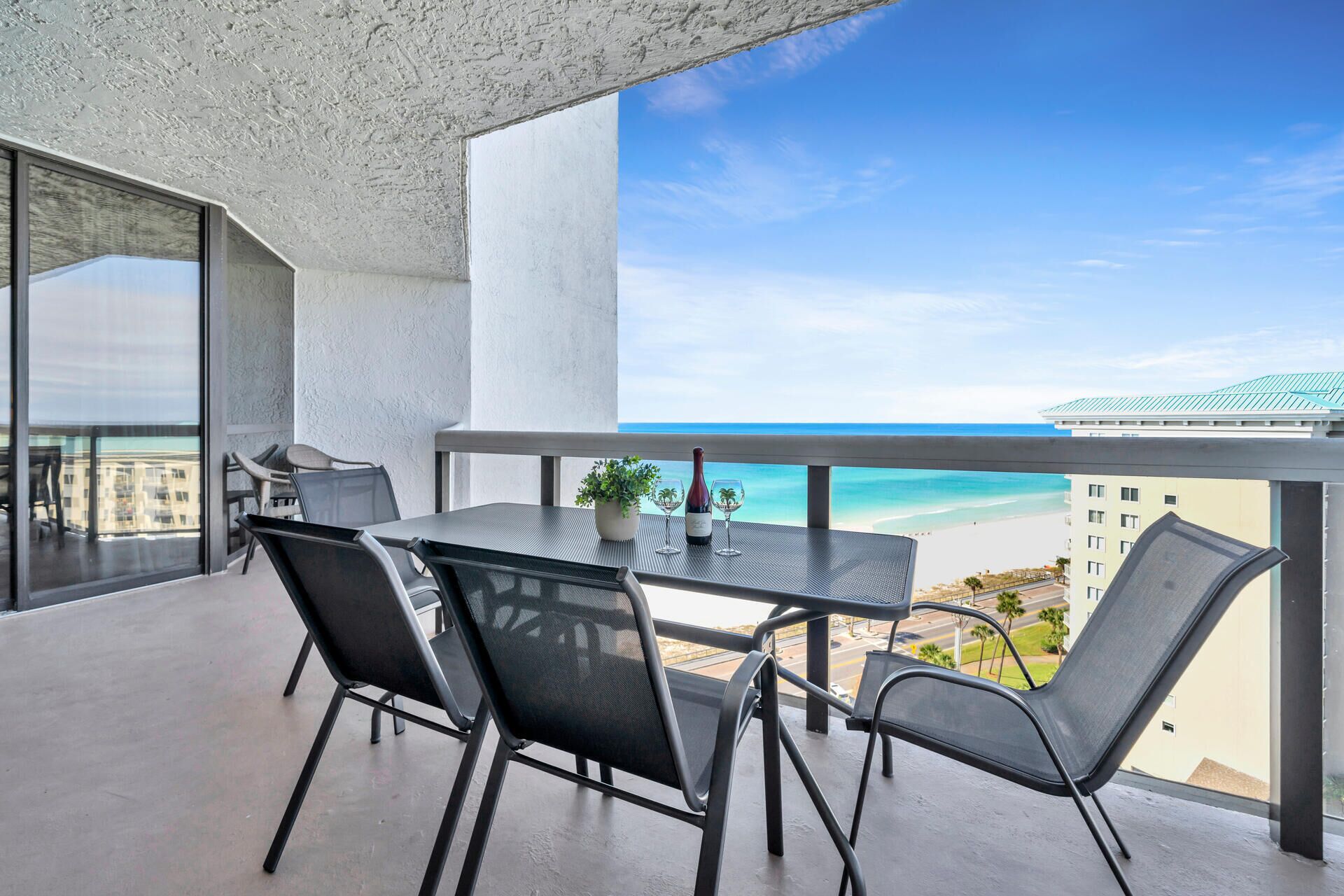 A balcony with a table and chairs, a bottle of wine, and a view of the beach and ocean.