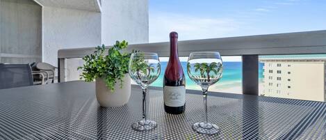 A balcony with a table, two wine glasses, a bottle of wine, and a potted plant.
