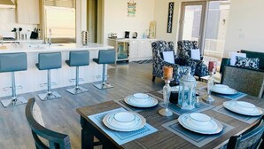 A modern kitchen with a central island, bar stools, and a dining area with a wooden table set for four.