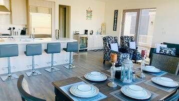 A modern kitchen with a central island, bar stools, and a dining area with a wooden table set for four.