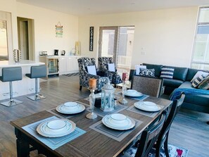 A dining area with a wooden table set for six, a sofa, and a chair in the background.