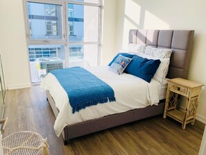 A bedroom with a bed, a window, and a small wooden nightstand.
