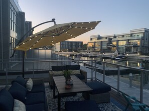 Terraza en la azotea con mobiliario exterior, una mesa con una planta y vistas a un puerto deportivo con barcos.