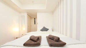Hotellihuone, jossa on sänky, kaksi pyyhettä, yöpöytä, lamppu ja ovi.