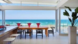 A modern dining area with a large table and chairs, a bar counter, and a view of the ocean. - Beachfront Hideaway (Sunrise Beach)