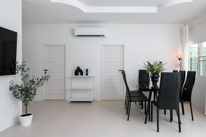 Un espace repas moderne avec un intérieur blanc, des chaises noires, une table centrale et une plante en pot.