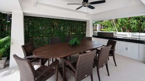 A modern dining area with a round table, wicker chairs, a ceiling fan, and a kitchen area with a sink and countertop.