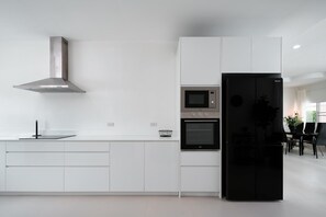 Une cuisine moderne avec des meubles blancs, une hotte en acier inoxydable, un four à micro-ondes, un four traditionnel et un réfrigérateur noir.