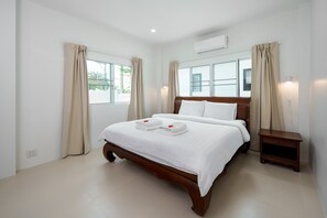 A hotel room with a large bed, two bedside tables, a nightstand, and an air conditioning unit.
