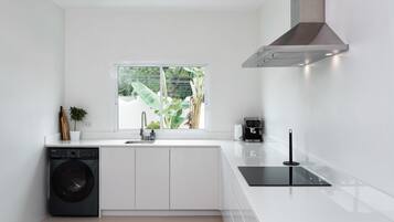 Una cocina moderna con lavadora integrada, ventana con vistas a la vegetación y una encimera negra elegante.