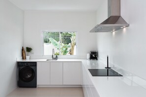 A modern kitchen with a built-in washer, a window with a view of greenery, and a sleek black countertop.