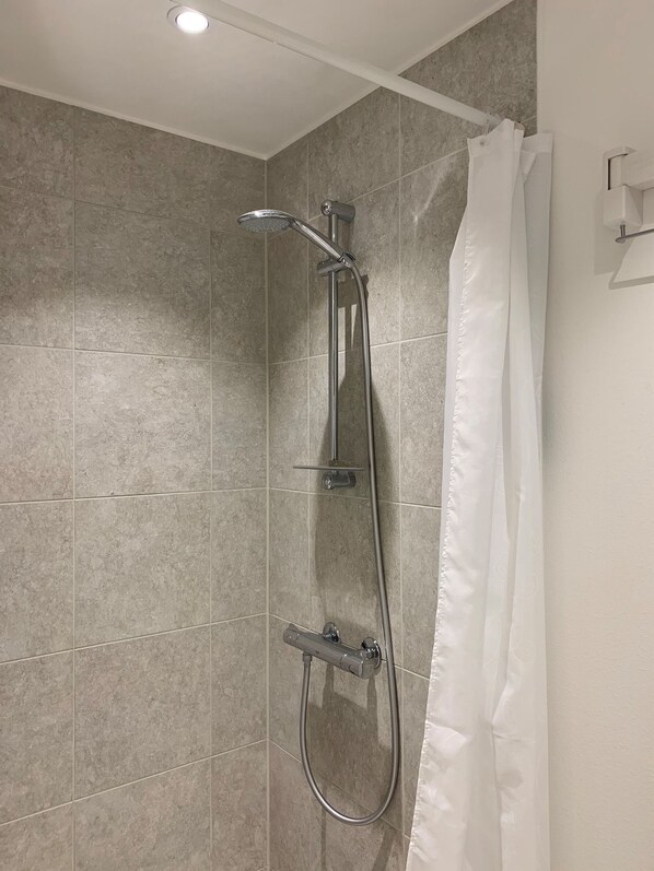 Un espace douche équipé d’un pommeau de douche à main et d’un pommeau de douche fixe, tous deux fixés sur un mur recouvert d’un pare-splash en carrelage.