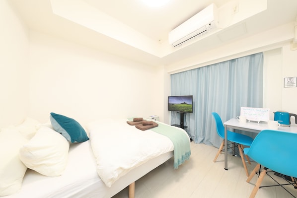 Habitación de hotel con cama, escritorio, silla, televisor y aire acondicionado.