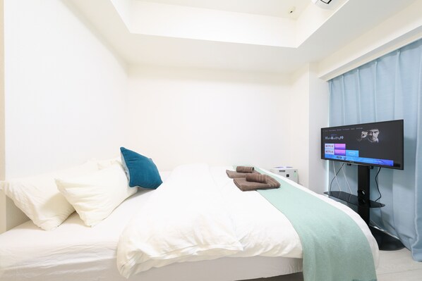 A hotel room with a bed, pillows, a blanket, a TV, and a window with curtains.