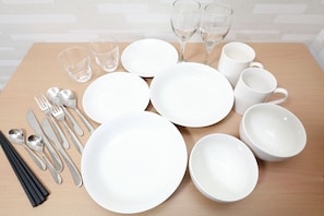 Una mesa dispuesta con platos blancos, tazones, tazas, cubiertos y copas de vino.