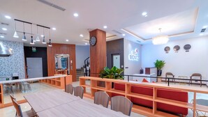 A modern hotel lobby with a long reception desk, multiple seating areas, and a staircase leading to an upper level.