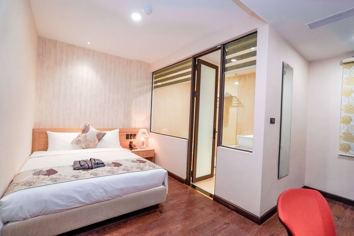 Un dormitorio con cama, mesita de noche, una silla roja y una puerta corredera que da al baño.