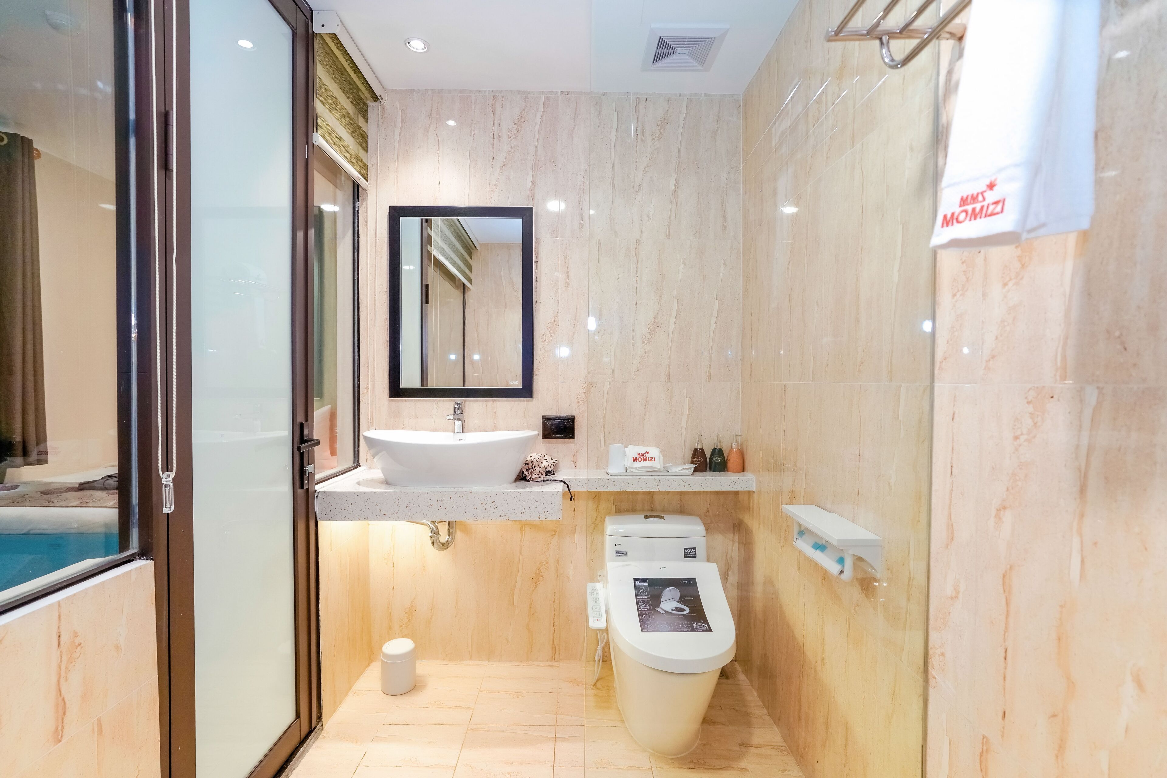 A modern bathroom with a glass shower enclosure, a sink with a mirror, a toilet with a digital display, and a towel hanging on a rack.