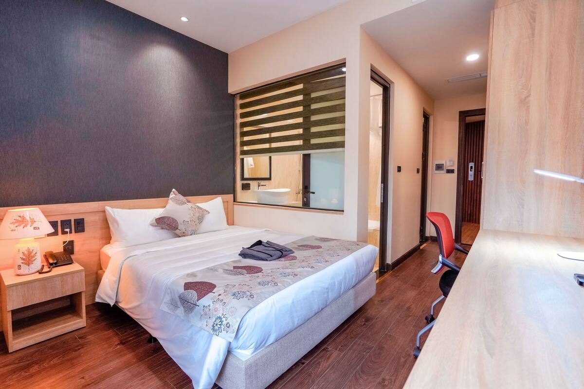 Habitación de hotel moderna con una cama grande, una mesita de noche con lámpara, un espejo y un escritorio con silla.