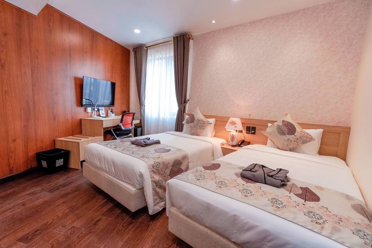 Habitación de hotel con dos camas, televisión, escritorio y ventana con cortinas.