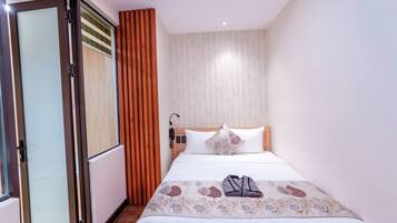 Een hotelkamer met een bed, een raam met zonwering, een houten hoofdeinde en een nachtkastje met een lamp.