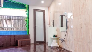 A bathroom with a wooden floor, a glass door, a shower area with a handheld showerhead, and a white sink with a mirror above it.