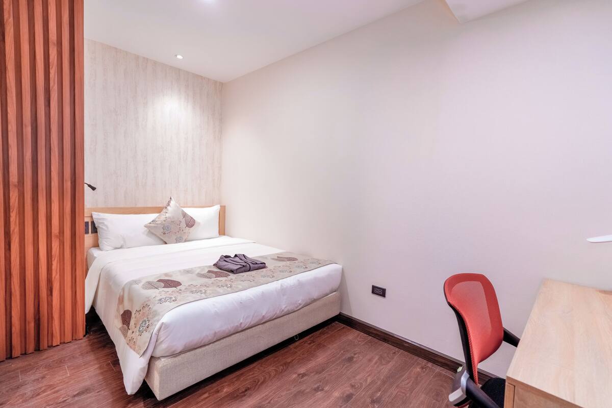 Un dormitorio ordenado con cama, una silla y un escritorio.