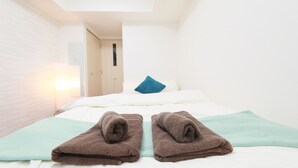 A hotel room with a bed, a blue pillow, and two brown towels on a light green bedspread. - IBASHO Shibuya Dogenzaka 907 (Tokyo)