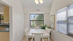 A dining area with a white table and chairs, a ceiling fan, a window with blinds, and a painting on the wall. - The Bungalow - Captiva Beach Cottage on Turner Beach (Captiva)