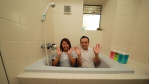 A bathtub with a showerhead, a window, and toiletries on the side. - IBASHO Shibuya Higashi 604 (Tokyo)