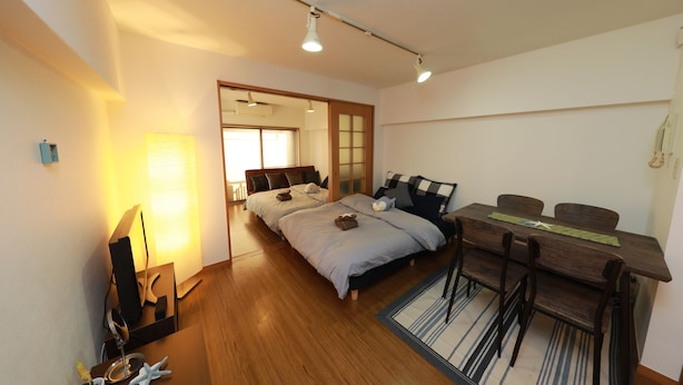 A bedroom with a wooden floor, a desk with chairs, a bed with pillows, and a lamp. - IBASHO Shibuya Higashi 604 (Tokyo)