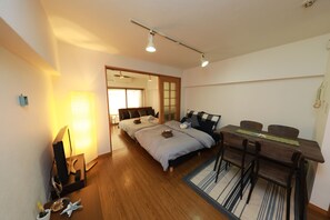 A bedroom with a wooden floor, a desk with chairs, a bed with pillows, and a lamp. - IBASHO Shibuya Higashi 604 (Tokyo)